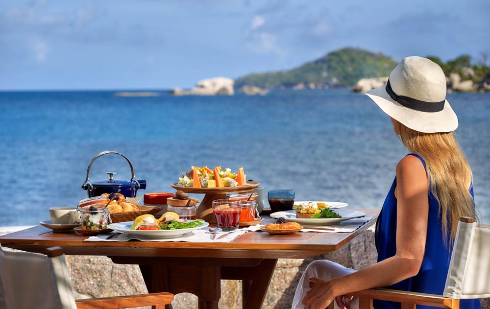 Frau geniesst ein Frühstück direkt am Meer
