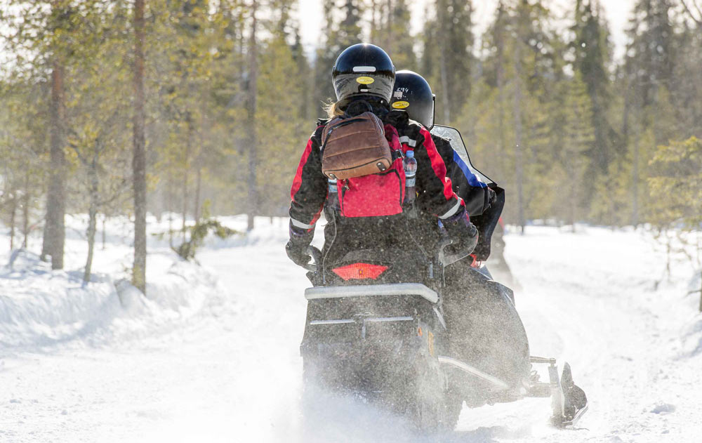 Zwei Personen auf einem Motorschlitten in einer Schneelandschaf
