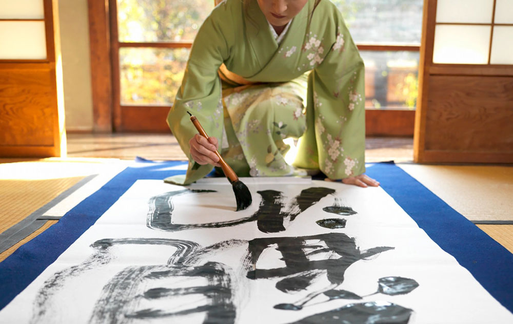 Asiatische Frau in einem traditionellen Kimono mit einem Pinsel in der Hand