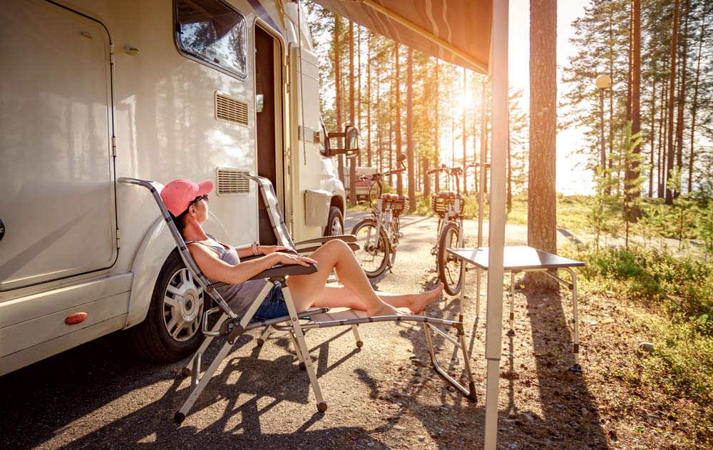 Frau geniesst den Sonnenuntergang in einem Stuhl neben Camper